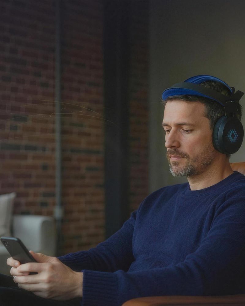 A Sens.ai member at home in an armchair, wearing the headset and reading his GeniusPulse Score on his phone